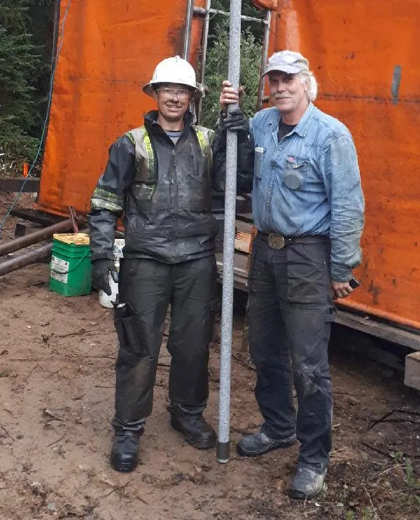 Two crew members holding a drill rod at a drill site