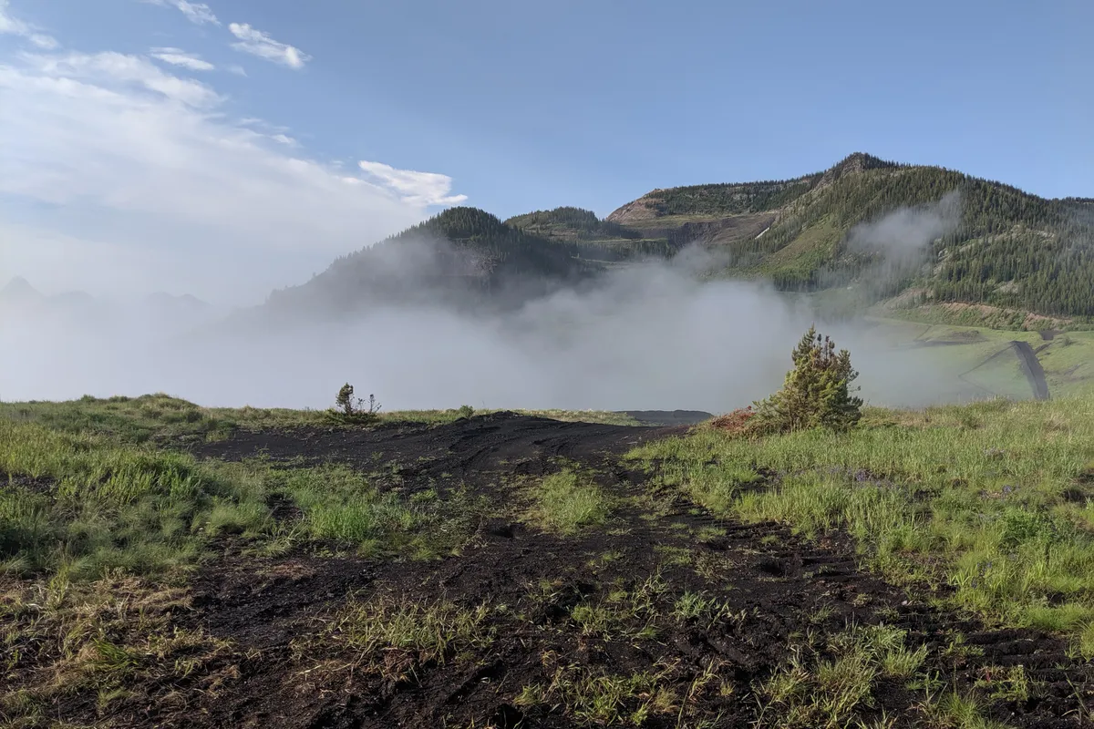 Reclaimed road regrowing with grass below a misty mountain